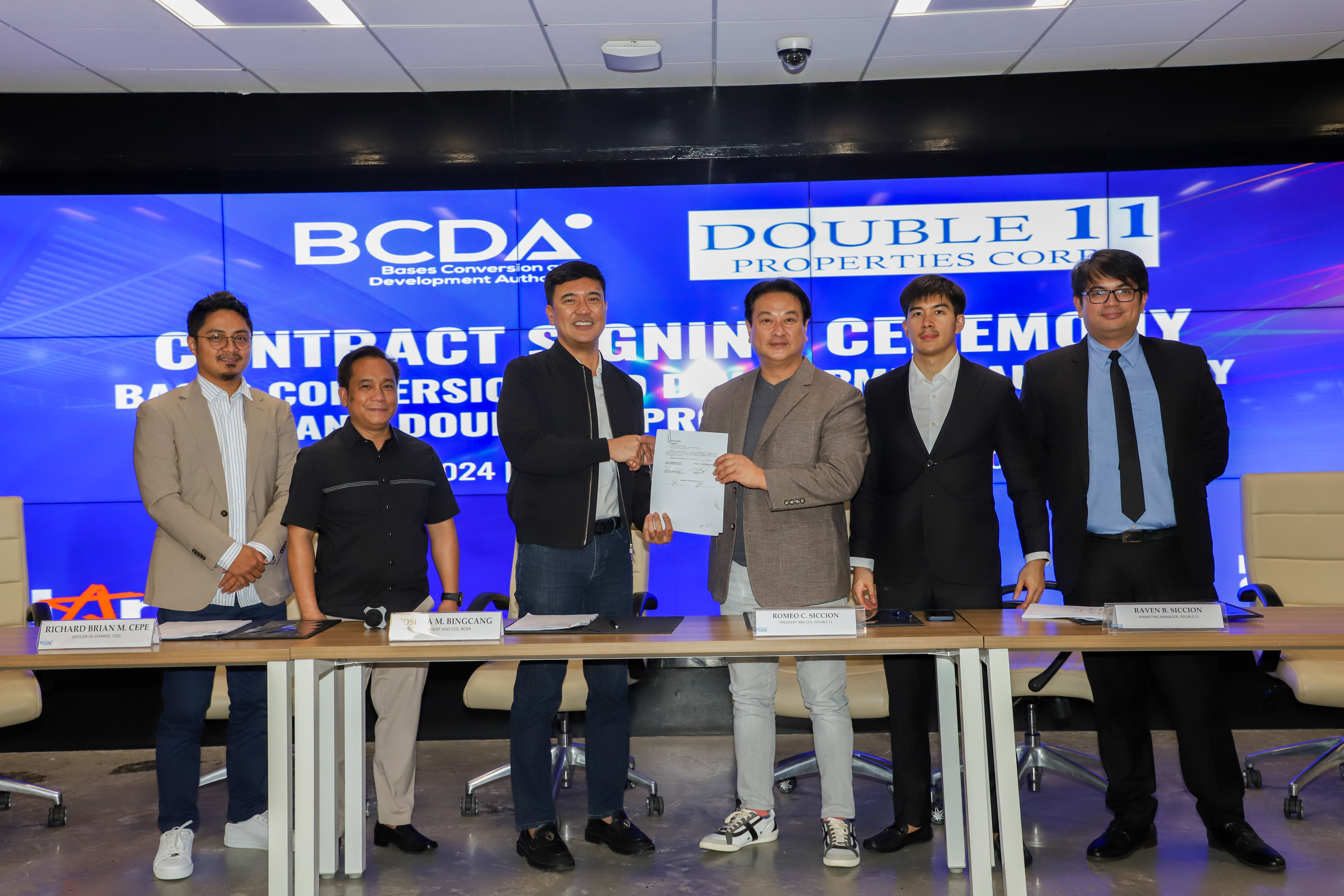 six people standing with two people in the center shaking hands holding the contract